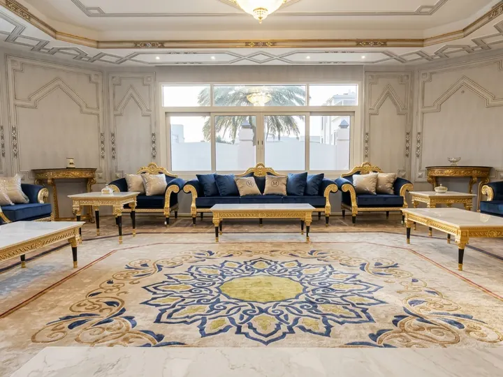 Gran salón de recepción con sofás azules y una alfombra de medallón en azul y oro sobre moqueta